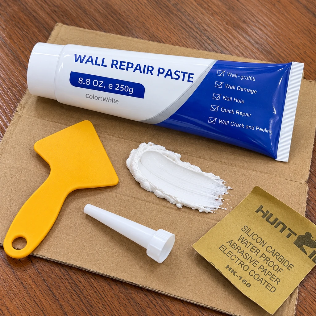 Wall repair paste tube with a white paste sample, yellow scraper, nozzle and sandpaper on cardboard