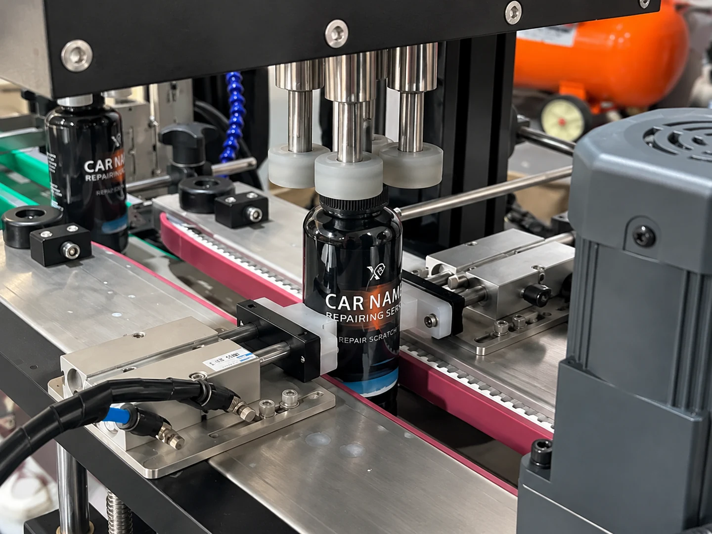 Capping machine heads positioned over black product bottles on a conveyor
