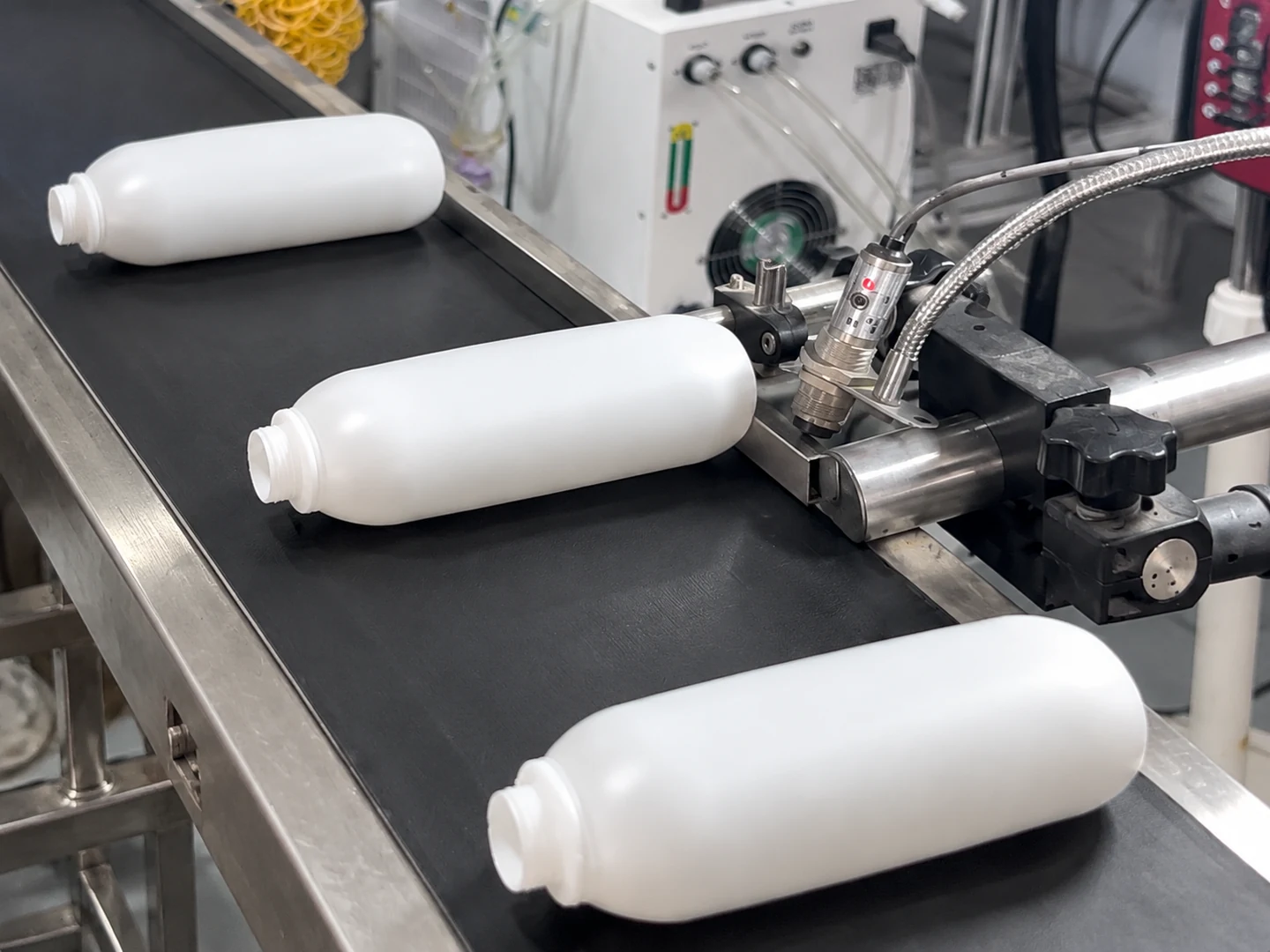 White bottles lying on a conveyor beside the bottle-base date coding station
