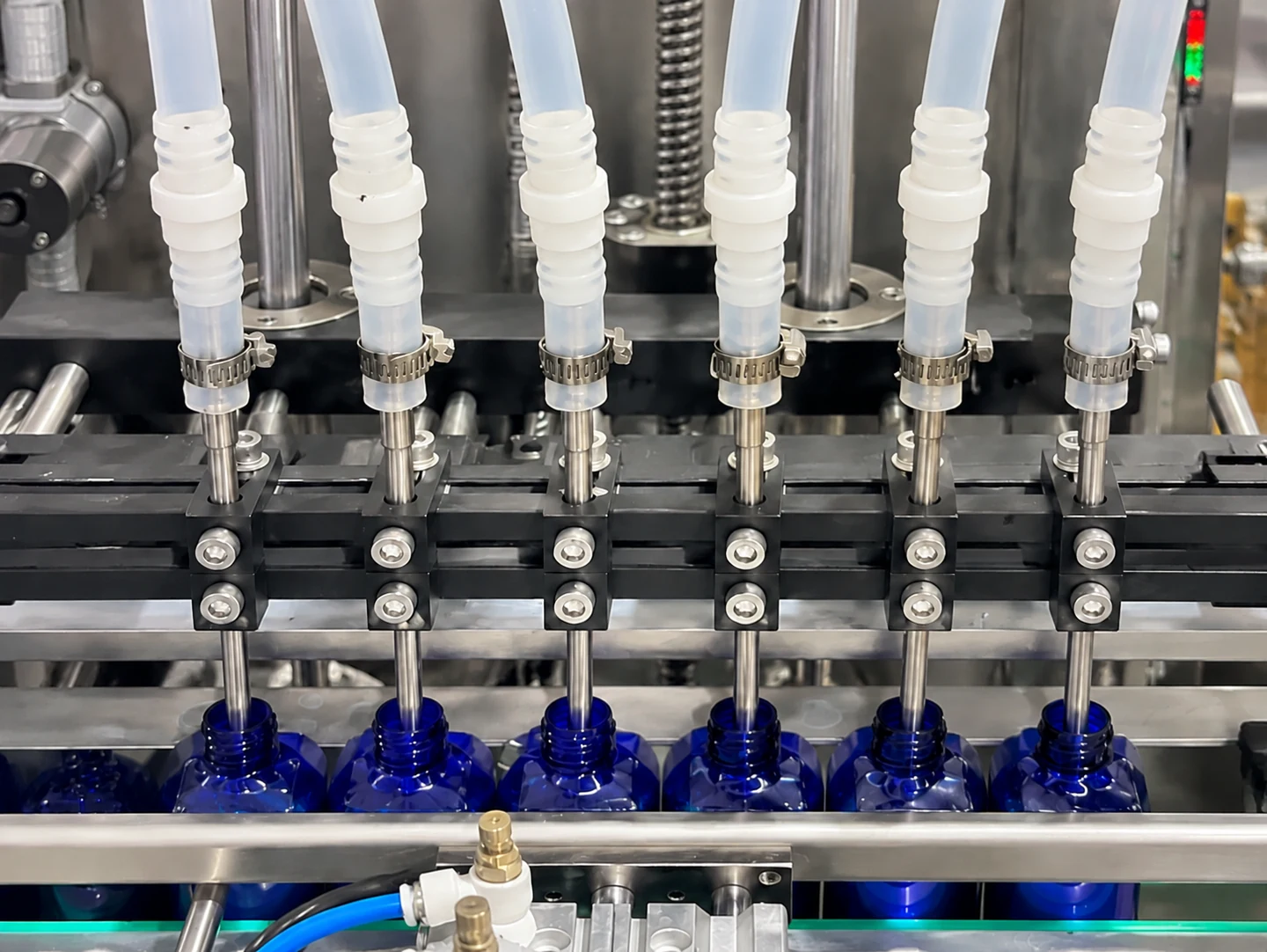 Multiple filling nozzles aligned with blue bottles on a liquid filling line
