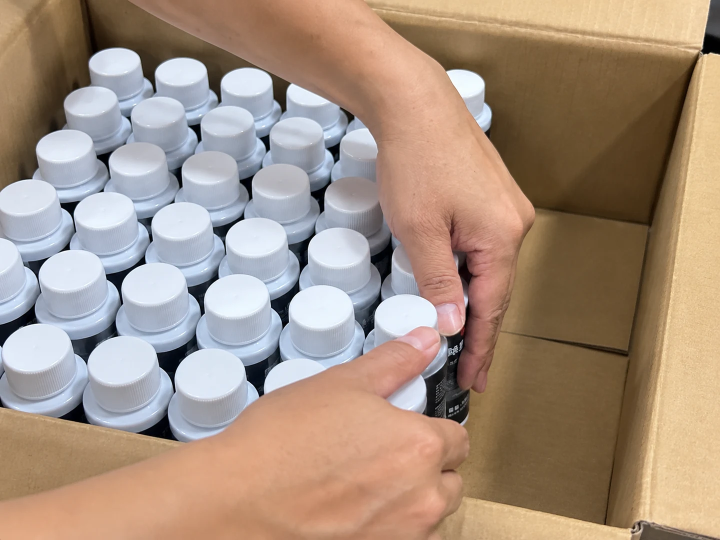 Hands arranging capped product bottles inside an open cardboard shipping carton